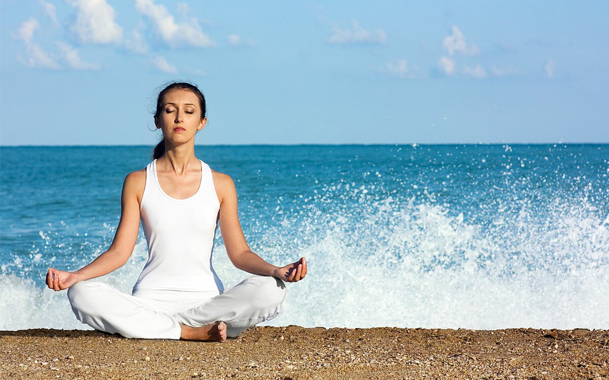 Лечением релаксации. Сурья бхедана пранаяма. Расслабление. Медитация на море. Девушка медитирует на берегу.